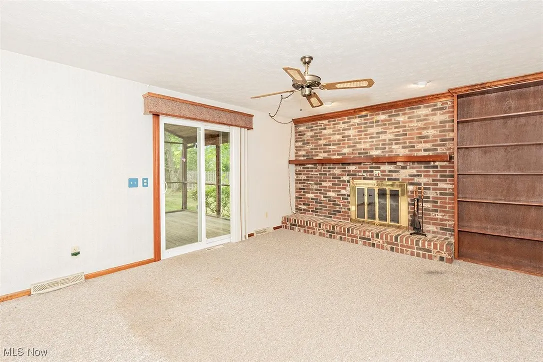 Unfurnished living room with a textured ceiling, carpet flooring, a brick fireplace, ceiling fan, and built in shelves