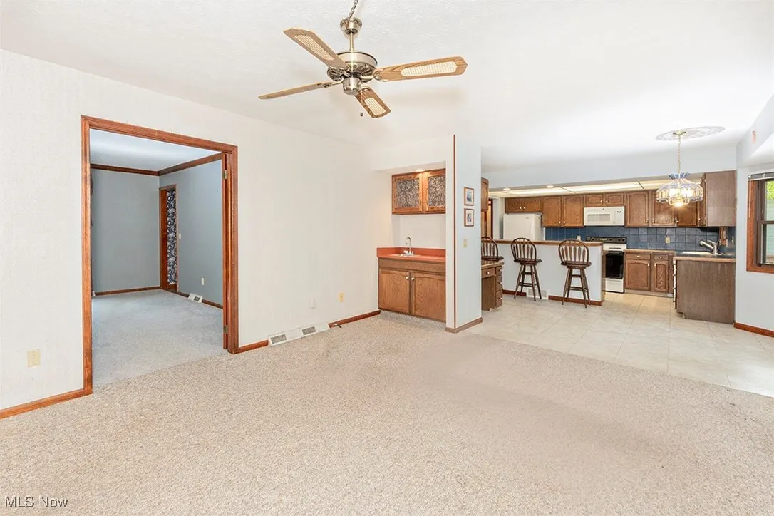 Unfurnished living room featuring light carpet, a ceiling fan, and light tile patterned flooring
