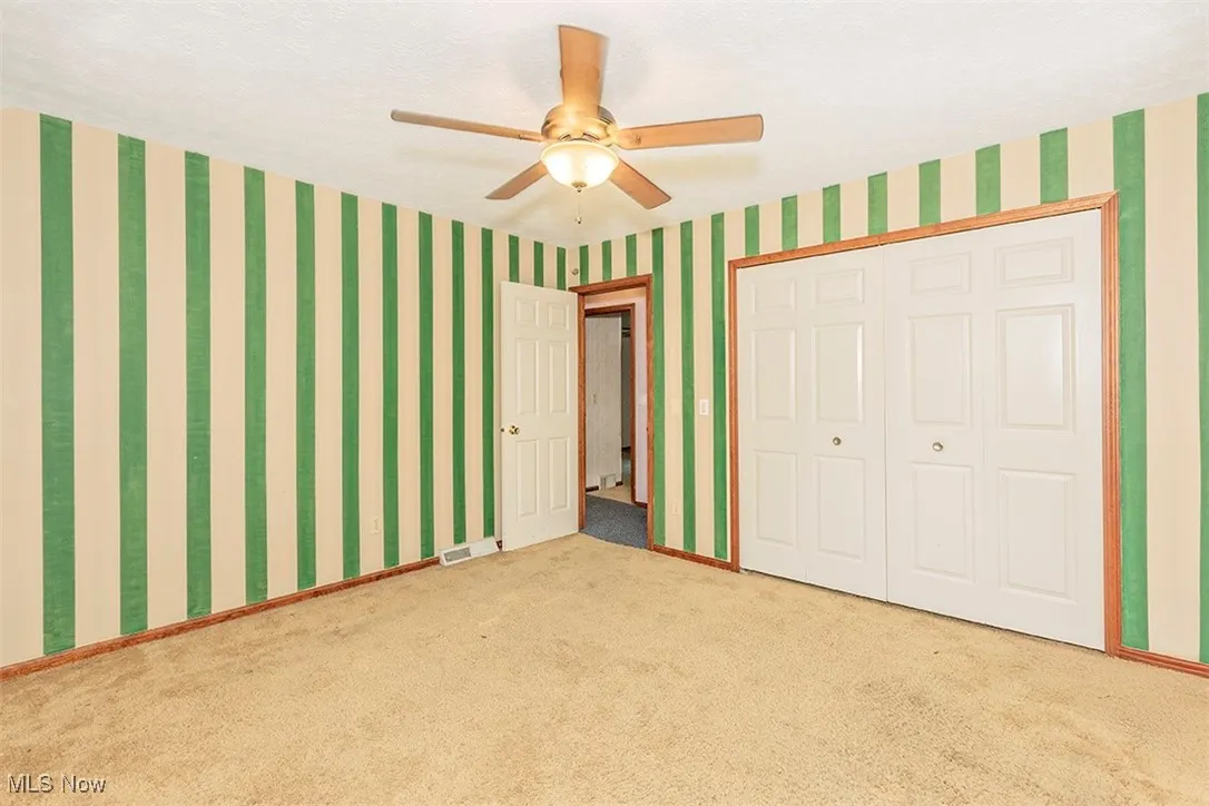 Unfurnished bedroom featuring wallpapered walls, carpet flooring, a ceiling fan, and a closet