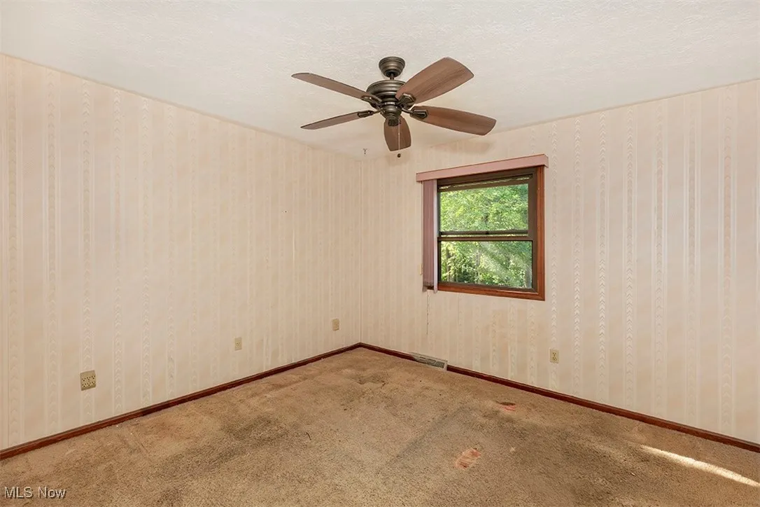 Spare room with a textured ceiling, carpet, wallpapered walls, and a ceiling fan