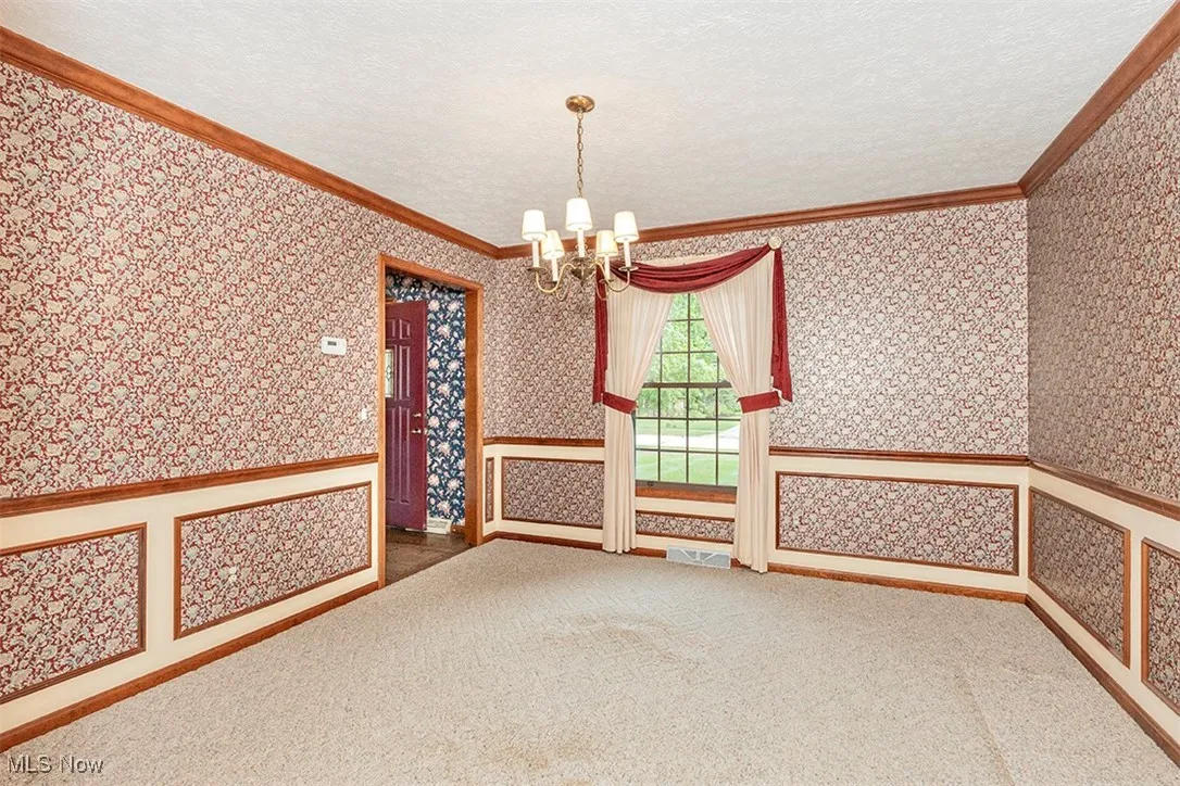 Spare room featuring crown molding, a chandelier, a textured ceiling, carpet, and wallpapered walls