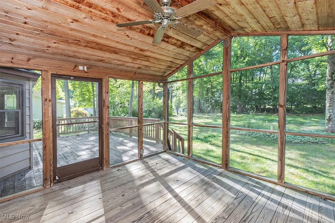 Unfurnished sunroom with vaulted ceiling, a wooden deck, and a ceiling fan