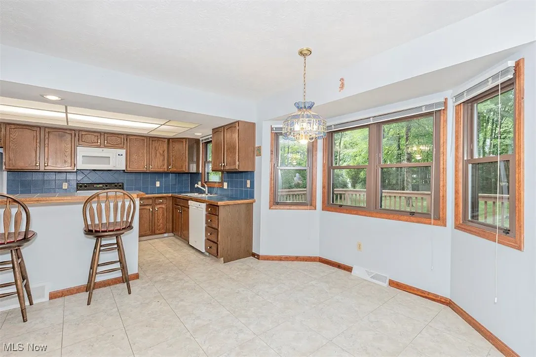 Kitchen with brown cabinets, backsplash, a breakfast bar area, pendant lighting, and a chandelier