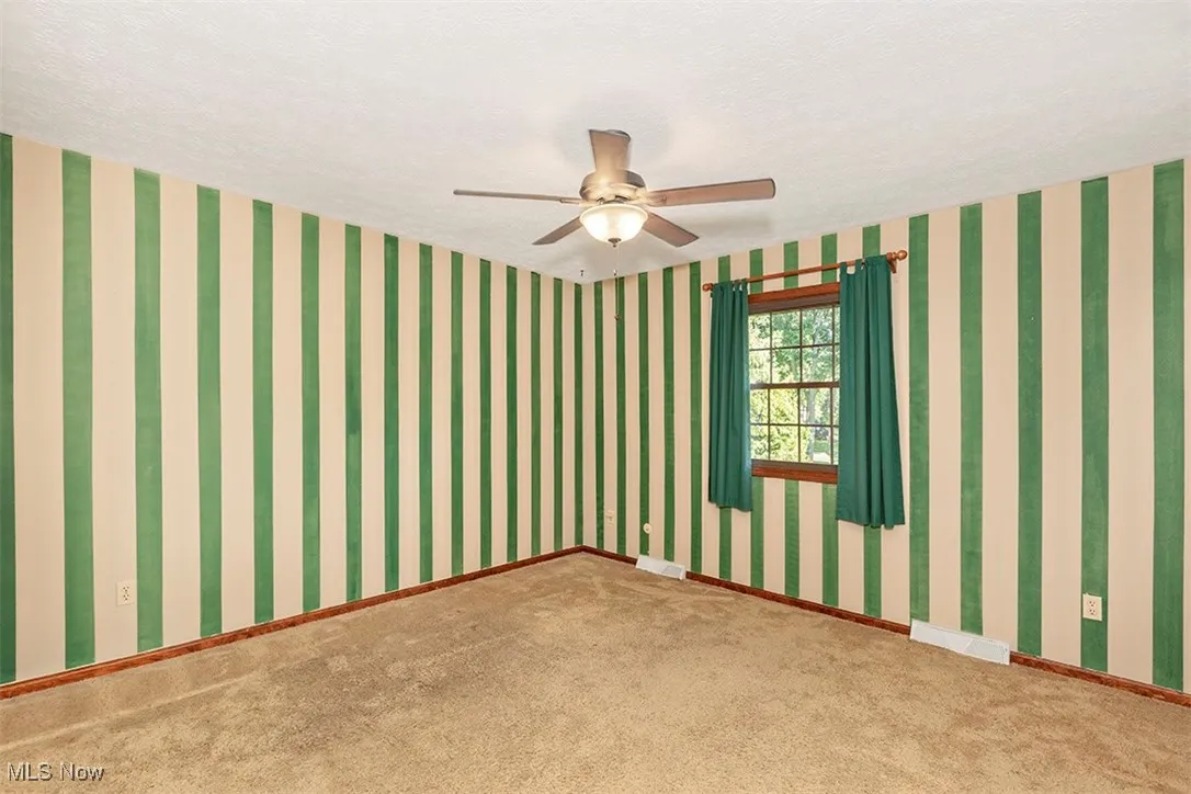 Unfurnished room featuring a textured ceiling, carpet, ceiling fan, and wallpapered walls
