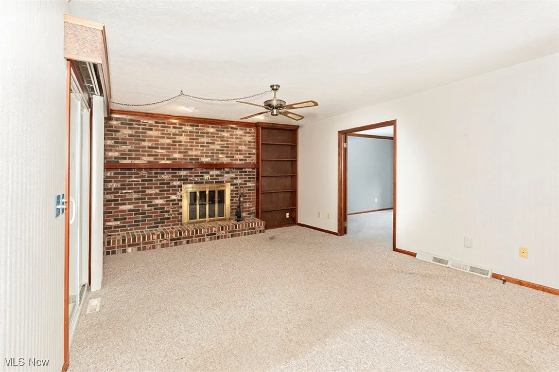 Unfurnished living room featuring a fireplace, built in shelves, carpet, a textured ceiling, and ceiling fan