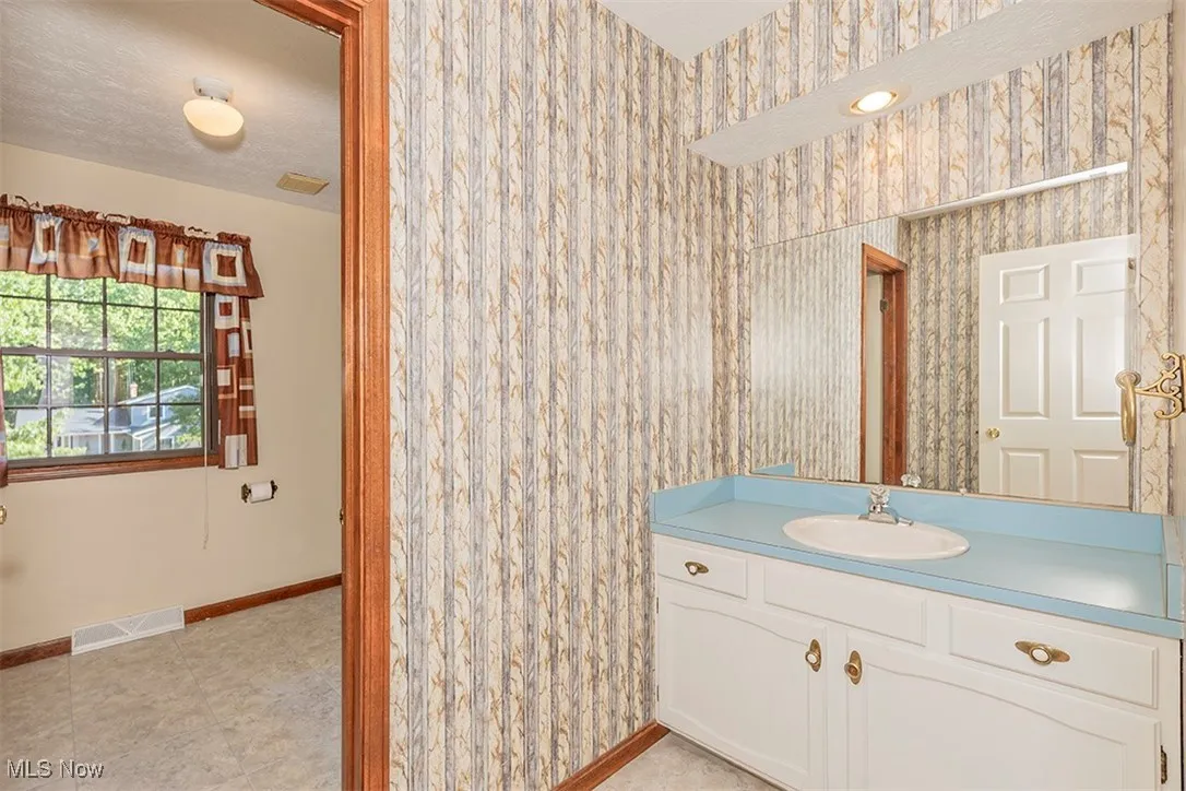 Bathroom with vanity, wallpapered walls, and light tile patterned flooring
