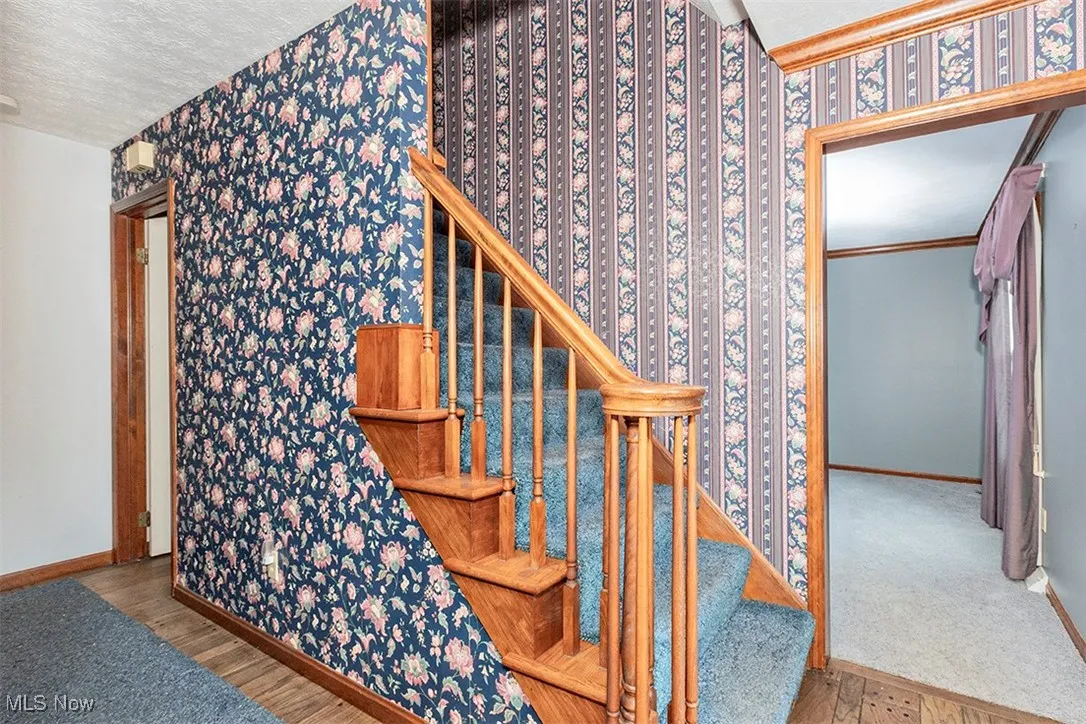 Stairway featuring wood finished floors, a textured ceiling, and wallpapered walls