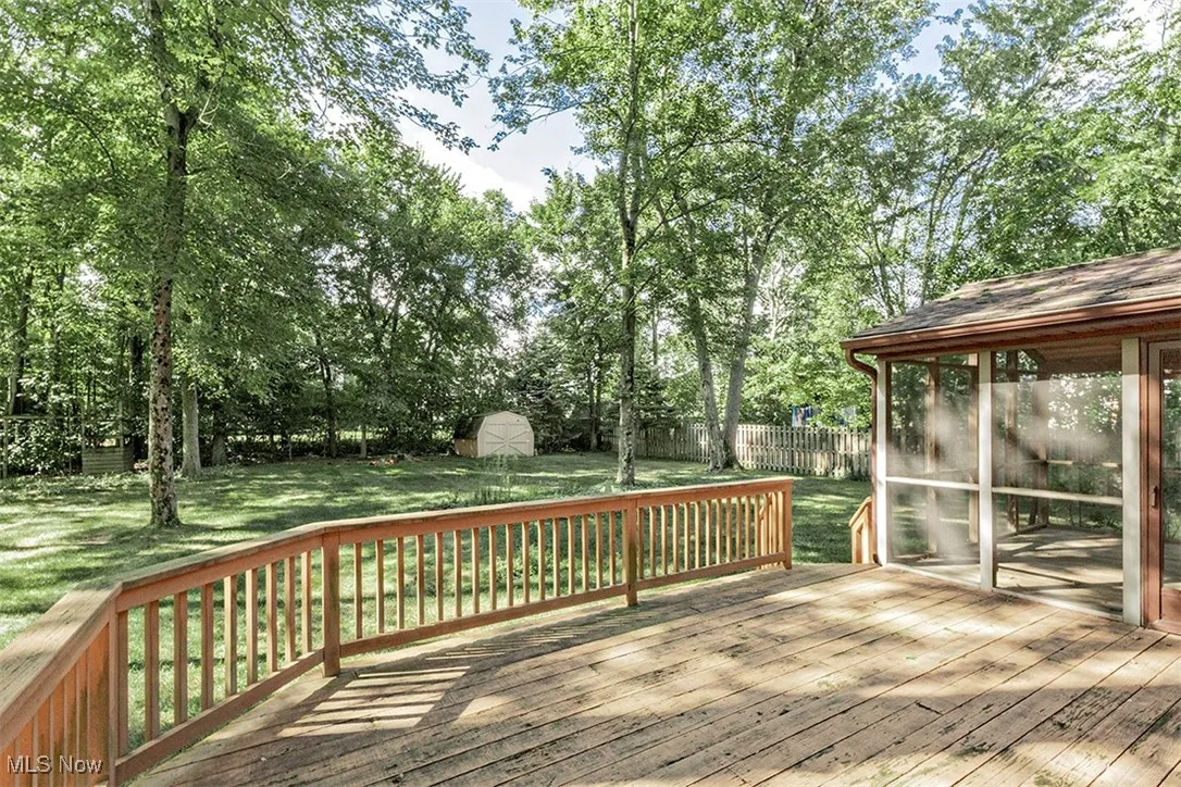 Deck featuring a sunroom, a fenced backyard, a shed, and view of wooded area
