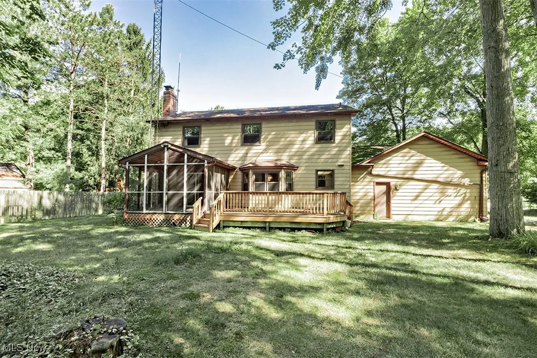 Back of property featuring a wooden deck, a sunroom, a chimney, and a lawn