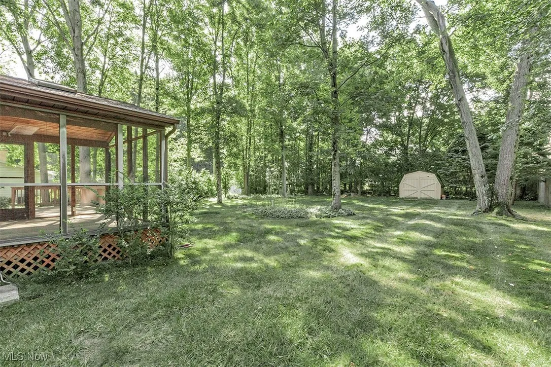 View of green lawn featuring a sunroom, a shed, and a wooden deck