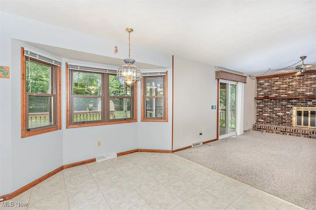 Unfurnished living room with carpet floors, a chandelier, a brick fireplace, and tile patterned floors