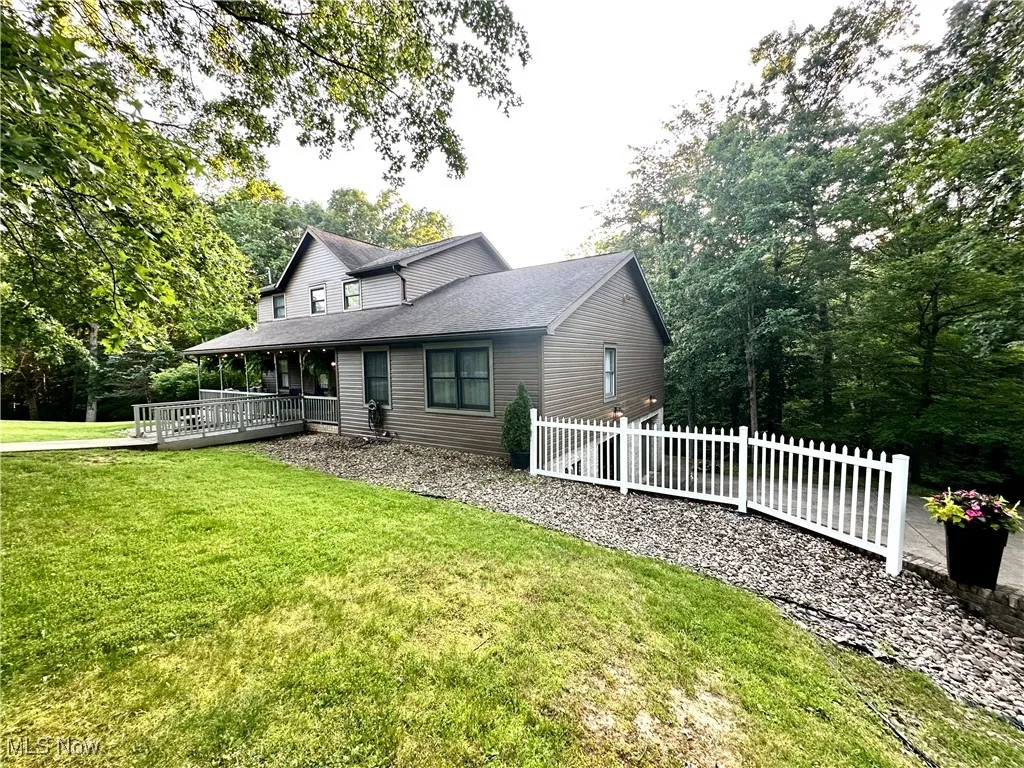 Farmhouse-style home featuring roof with shingles, view of scattered trees, and a wooden deck