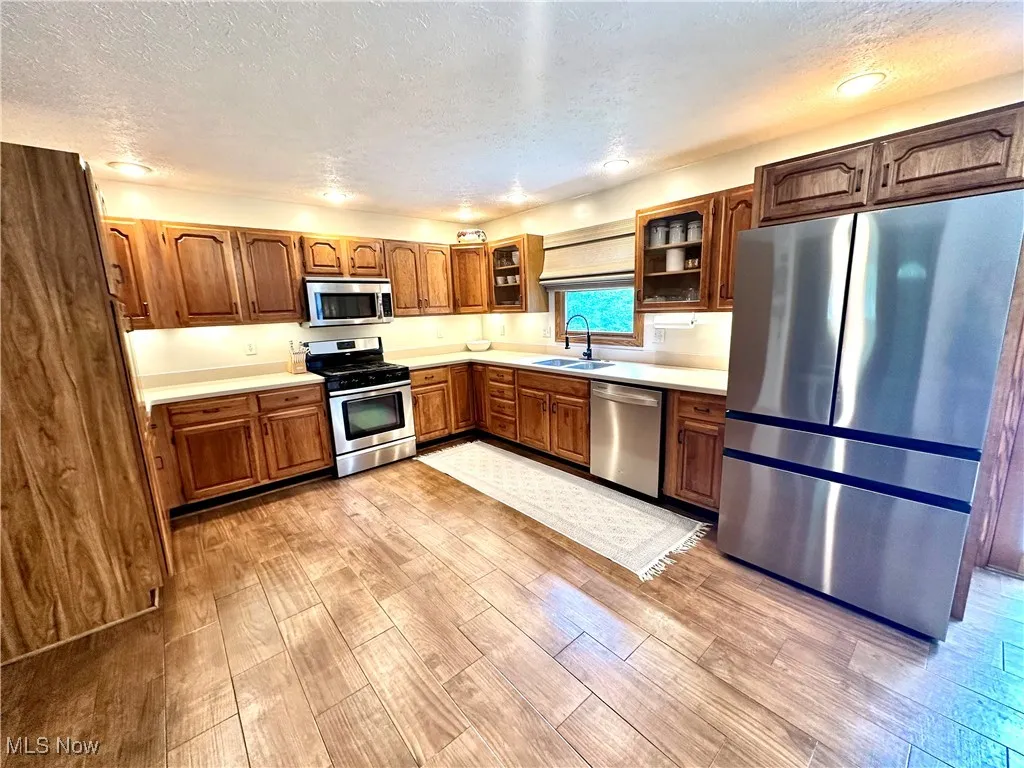 Kitchen featuring stainless steel appliances, light countertops, glass insert cabinets, a textured ceiling, and light wood-style flooring