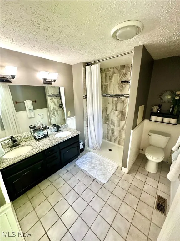 Bathroom featuring light tile patterned floors, a shower stall, double vanity, and a textured ceiling