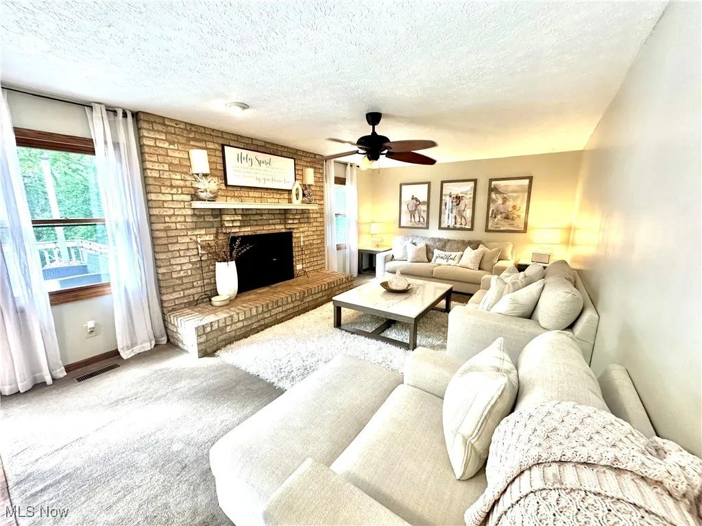 Living area featuring carpet floors, a textured ceiling, a ceiling fan, and a fireplace