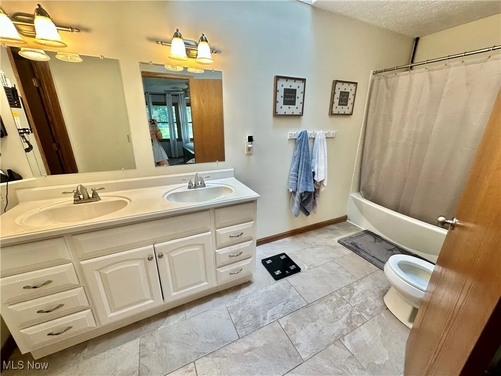 Full bathroom featuring shower / bath combo, double vanity, and a textured ceiling