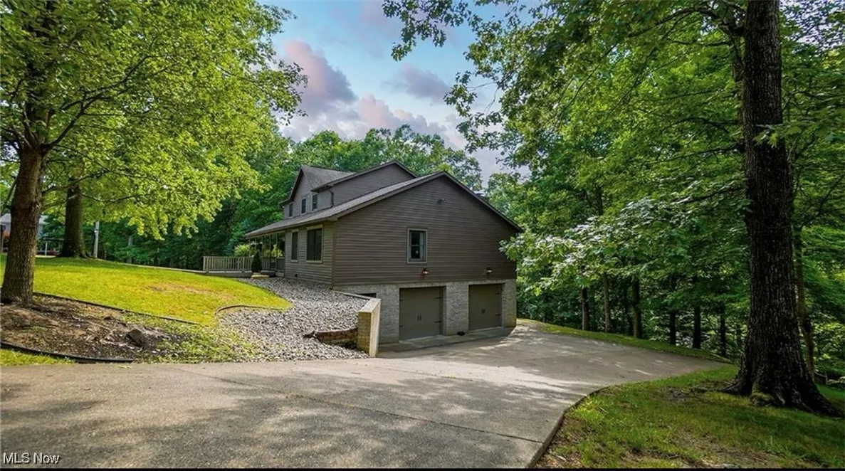 View of side of property with a garage, a yard, concrete driveway, and view of scattered trees