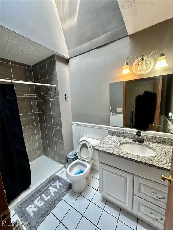 Full bathroom featuring a textured ceiling, vanity, a stall shower, light tile patterned flooring, and wainscoting