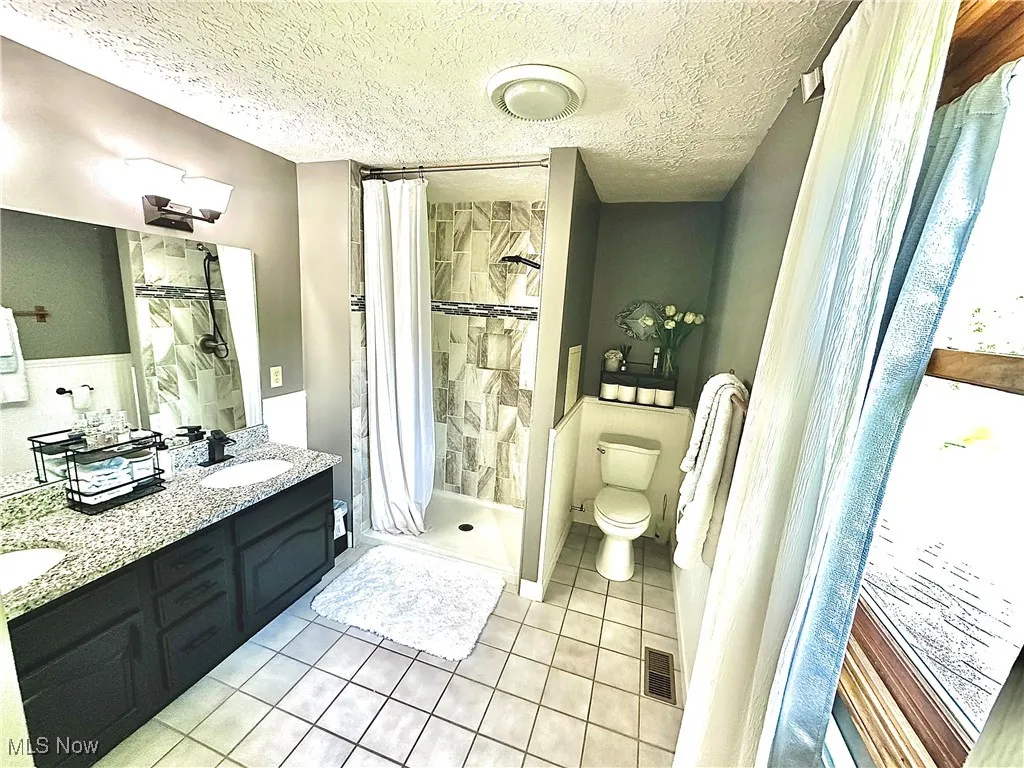 Full bath featuring light tile patterned floors, a shower stall, double vanity, and a textured ceiling