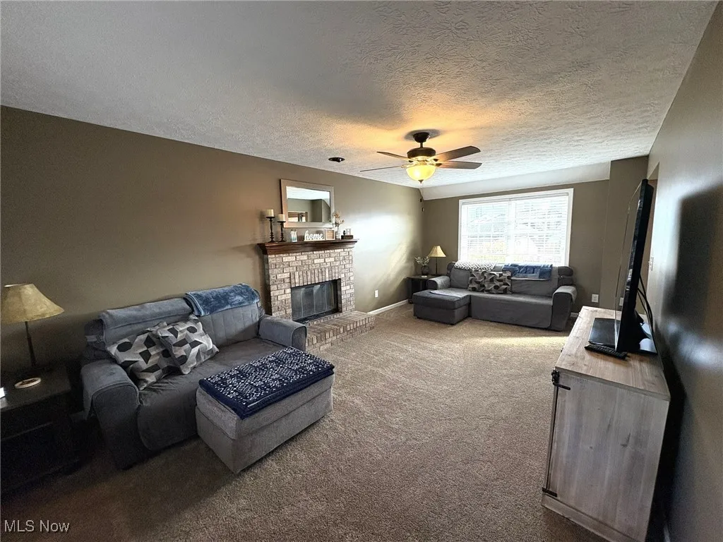 Carpeted living area featuring a ceiling fan, a textured ceiling, and a brick fireplace