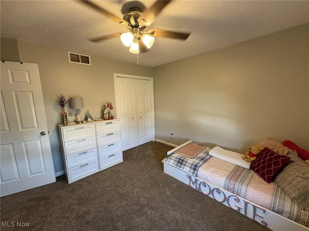 Bedroom featuring a textured ceiling, dark colored carpet, a ceiling fan, and a closet