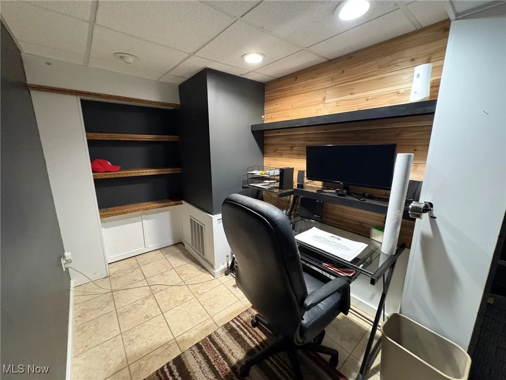 Office with a paneled ceiling, light tile patterned floors, and wood walls
