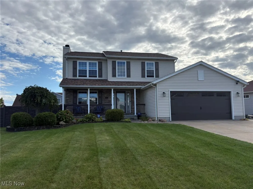 Traditional home featuring covered porch, an attached garage, a chimney, and driveway