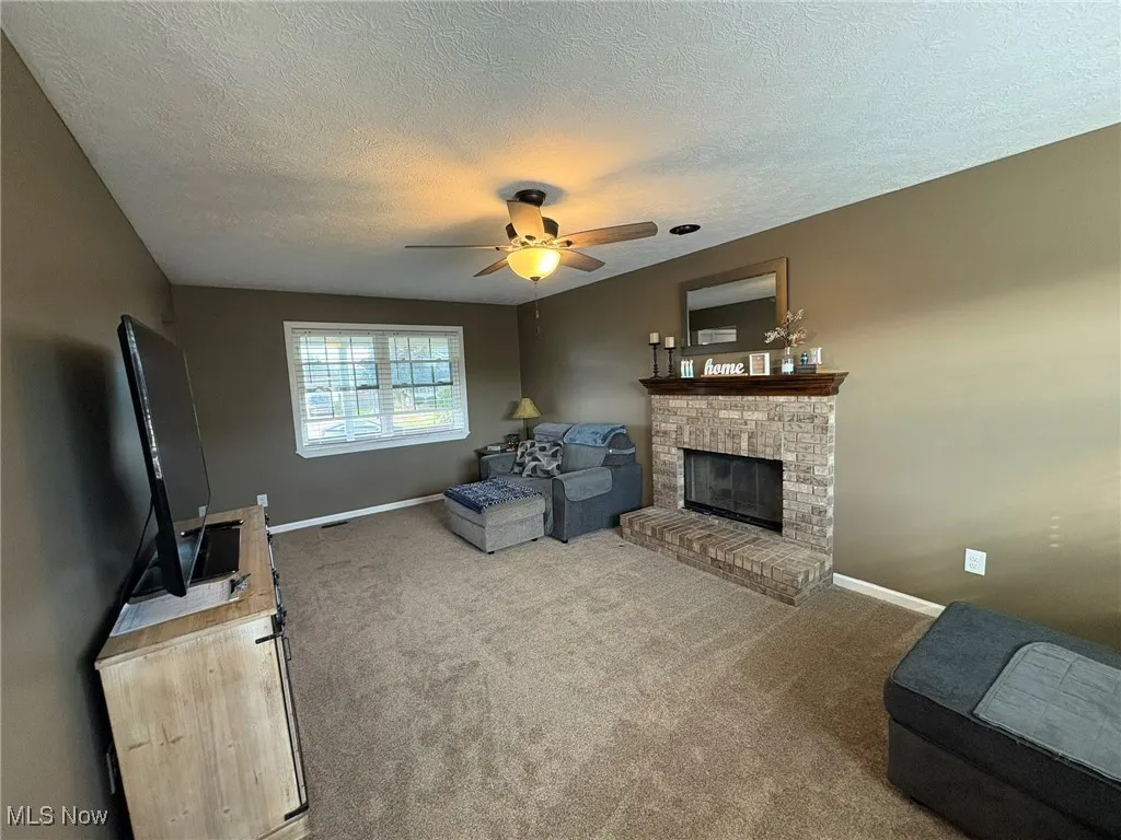 Carpeted living area with a brick fireplace, a textured ceiling, and a ceiling fan
