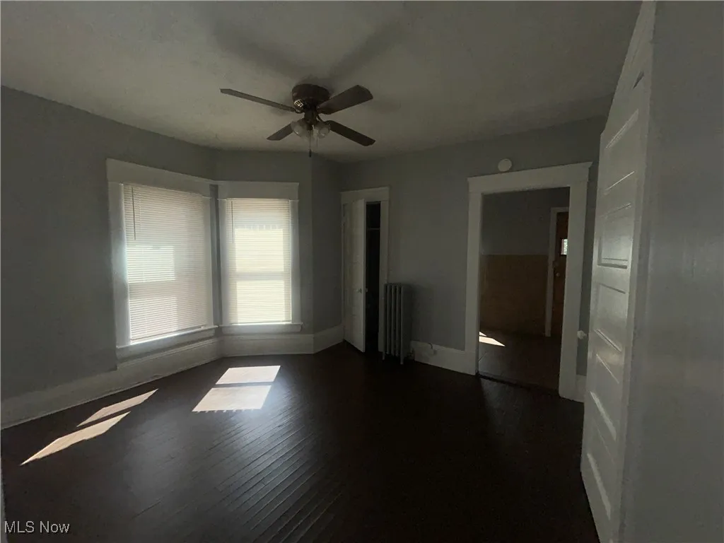 Unfurnished bedroom with dark wood-type flooring, ceiling fan, and radiator heating unit