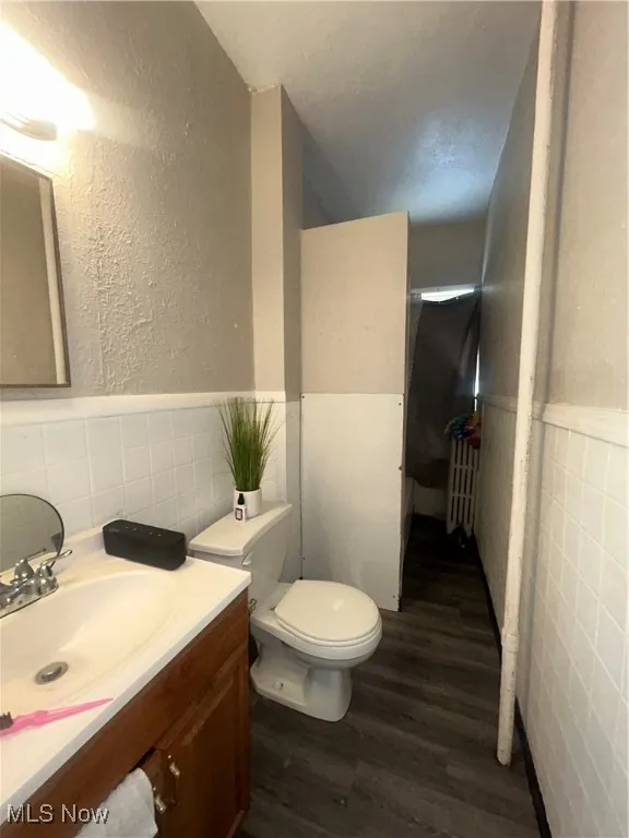 Full bath featuring tile walls, a wainscoted wall, a textured wall, vanity, and dark wood finished floors