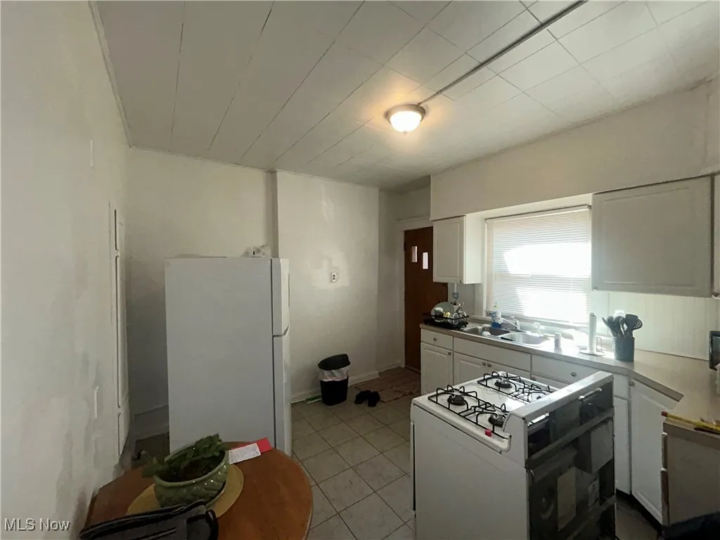 Kitchen featuring white cabinetry, white appliances, light tile patterned flooring, and light countertops