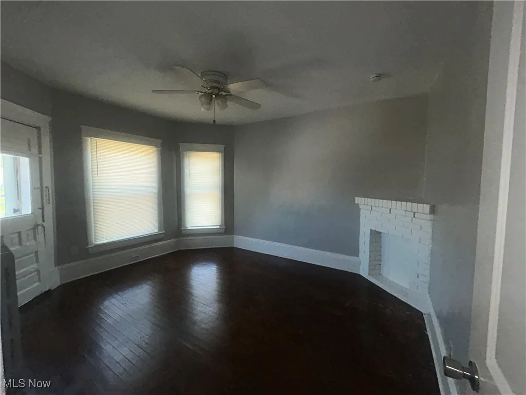 Unfurnished living room featuring dark wood finished floors, a fireplace, and a ceiling fan