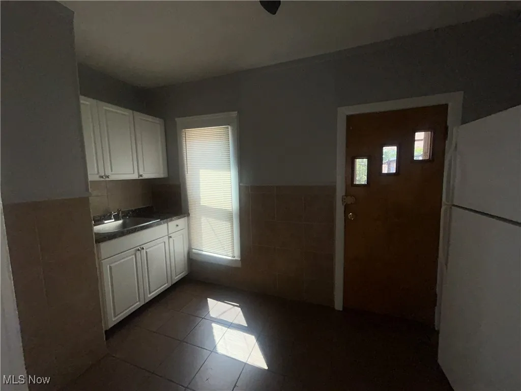 Kitchen featuring tile walls, white cabinetry, freestanding refrigerator, dark tile patterned flooring, and a wainscoted wall