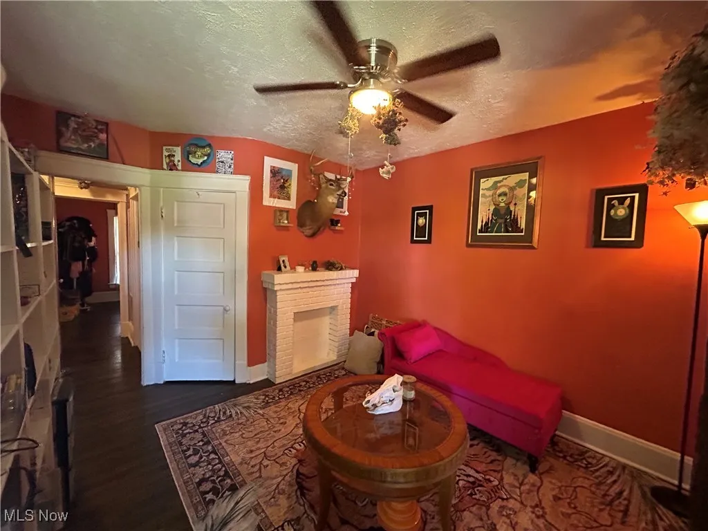 Living area featuring a brick fireplace, a textured ceiling, dark wood-type flooring, and a ceiling fan
