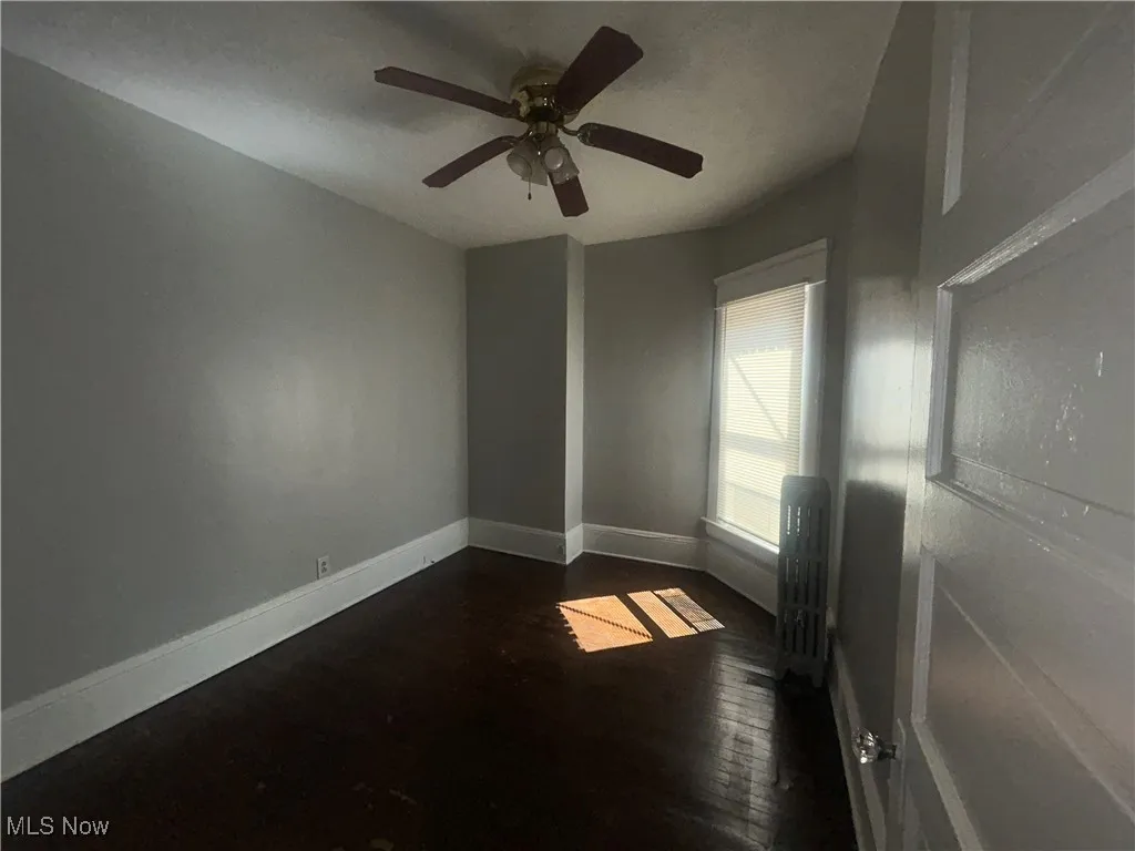 Empty room featuring dark wood-style floors, radiator heating unit, and a ceiling fan