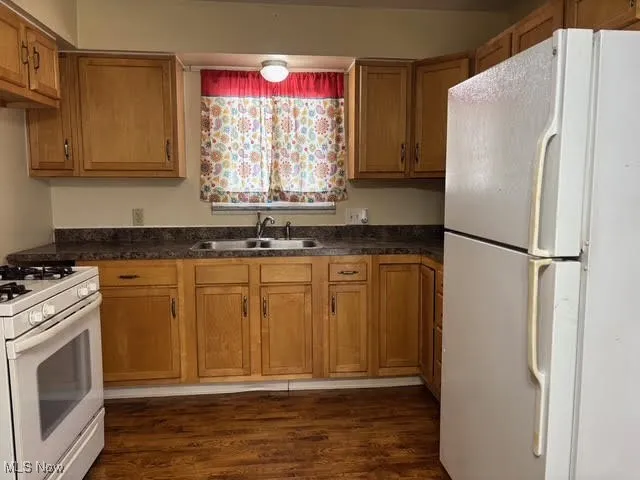 Kitchen with white appliances, brown cabinets, dark countertops, and dark wood-style flooring