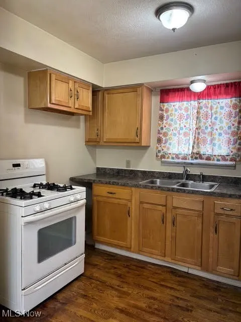 Kitchen with gas range gas stove, dark wood-type flooring, brown cabinets, dark countertops, and a textured ceiling