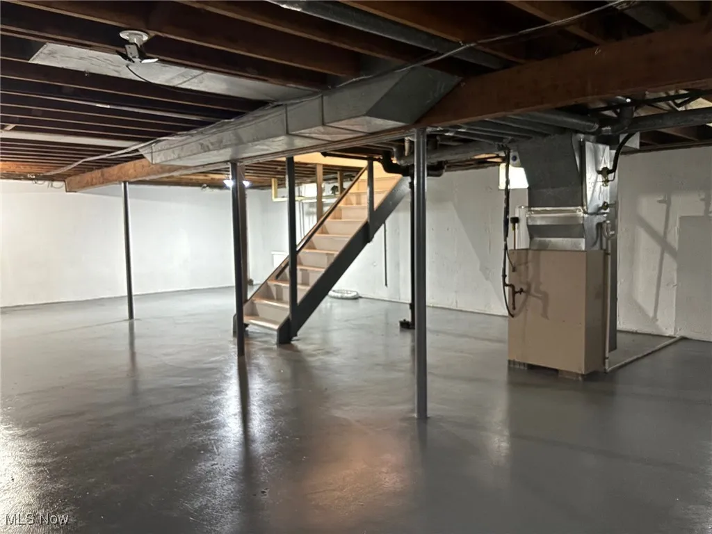 Unfinished below grade area featuring heating unit and stairway