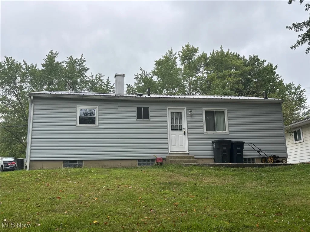 Rear view of property with entry steps, a metal roof, and a yard