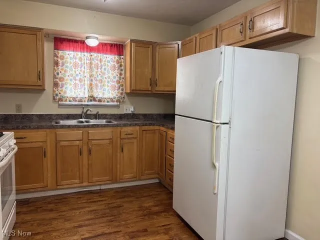 Kitchen with freestanding refrigerator, dark wood-style flooring, stainless steel stove, and brown cabinets