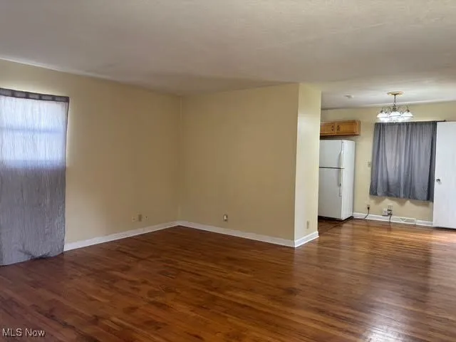 Unfurnished living room with dark wood-style floors and a chandelier