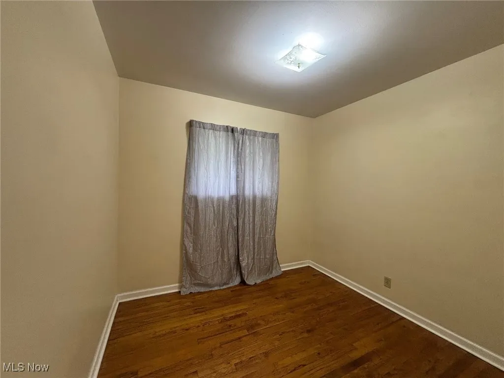 Spare room with dark wood-type flooring and baseboards