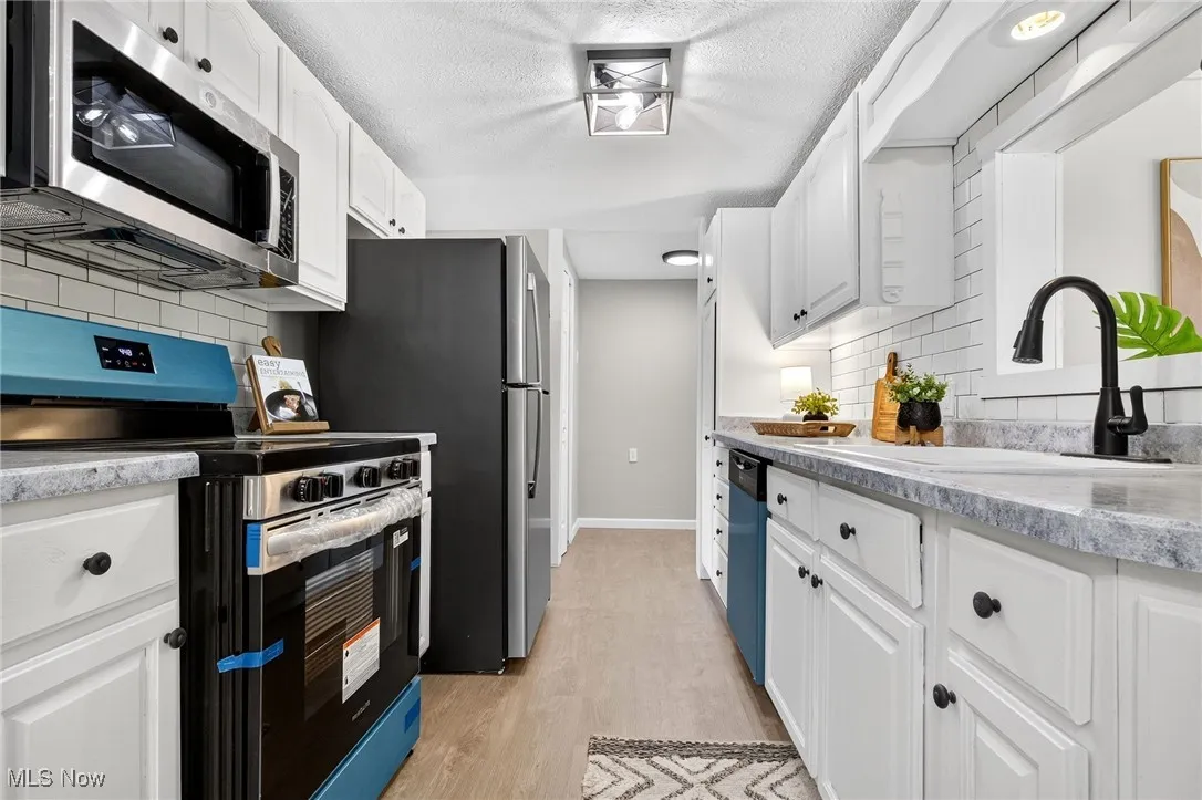 Kitchen featuring stainless steel appliances, decorative backsplash, white cabinets, light wood-style floors, and a textured ceiling