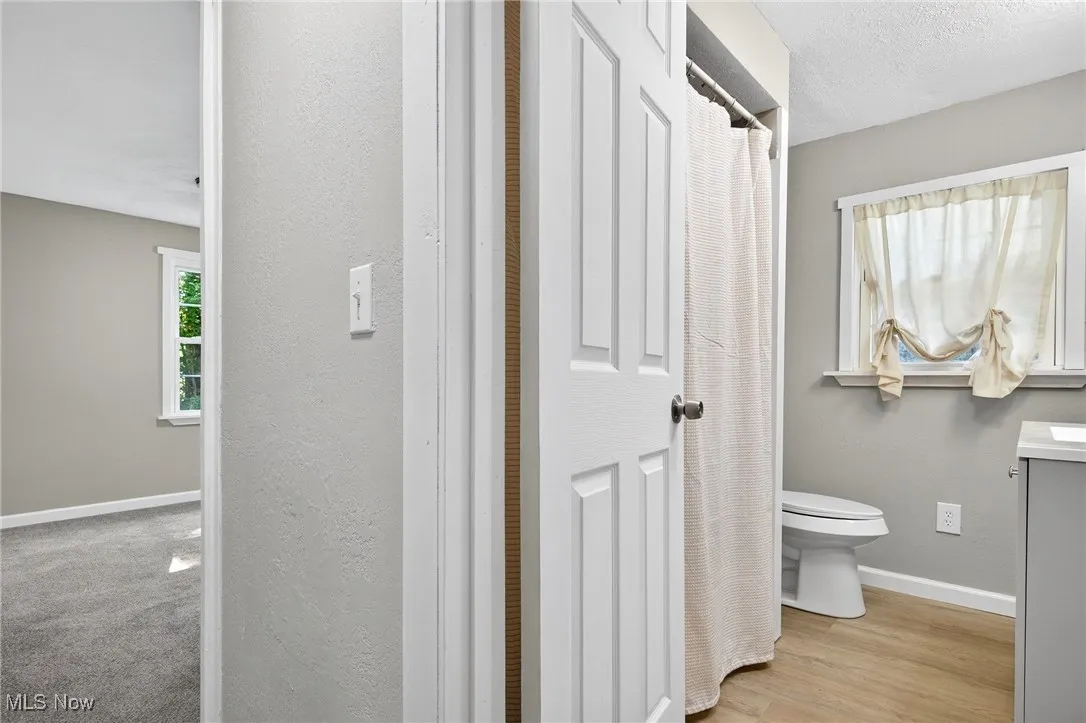 Bathroom featuring a shower with curtain, vanity, light wood finished floors, a textured wall, and a textured ceiling
