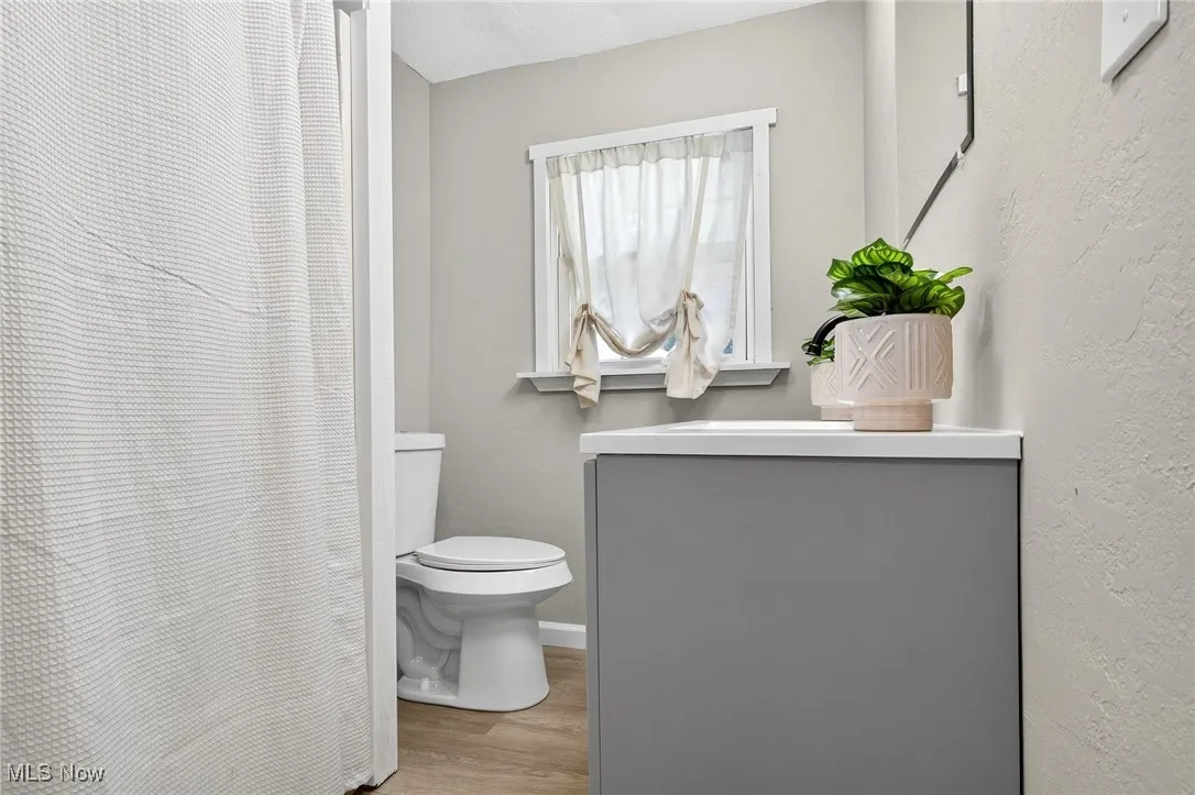 Bathroom with vanity, light wood-style floors, curtained shower, and a textured wall
