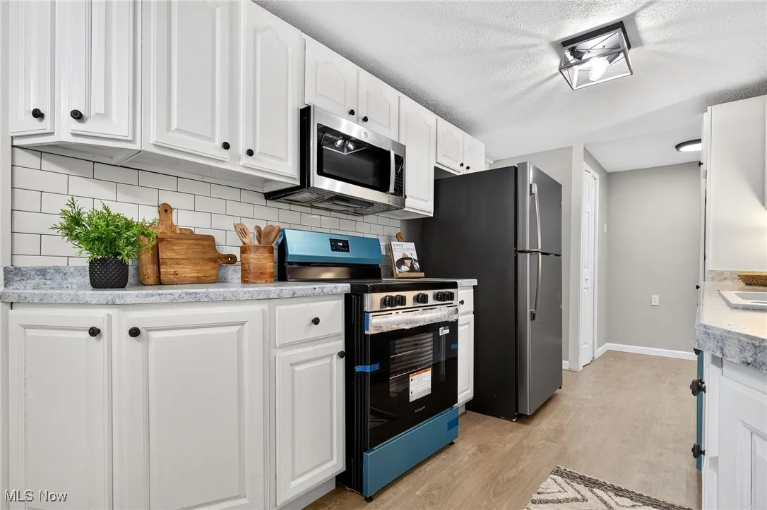 Kitchen with stainless steel appliances, white cabinetry, light wood-style floors, light countertops, and tasteful backsplash