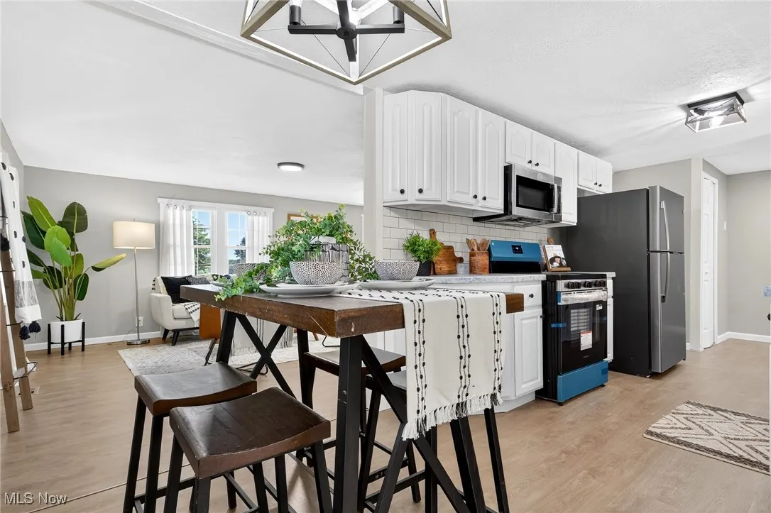 Kitchen with white cabinetry, stainless steel appliances, light countertops, backsplash, and light wood-type flooring