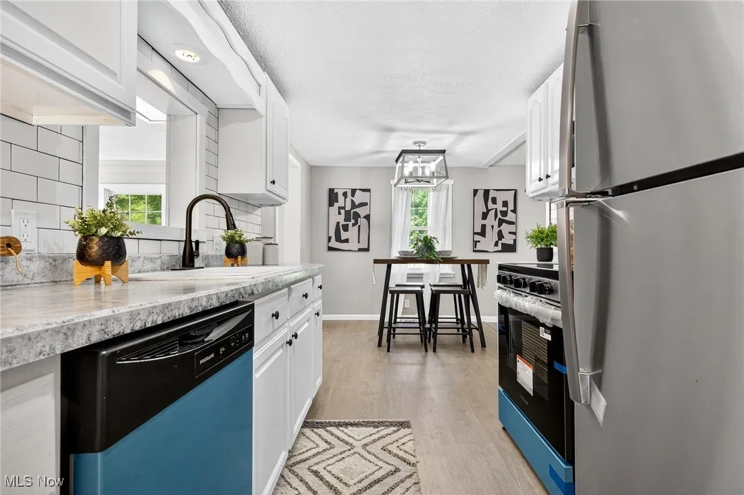 Kitchen featuring freestanding refrigerator, dishwasher, white cabinets, light wood finished floors, and tasteful backsplash