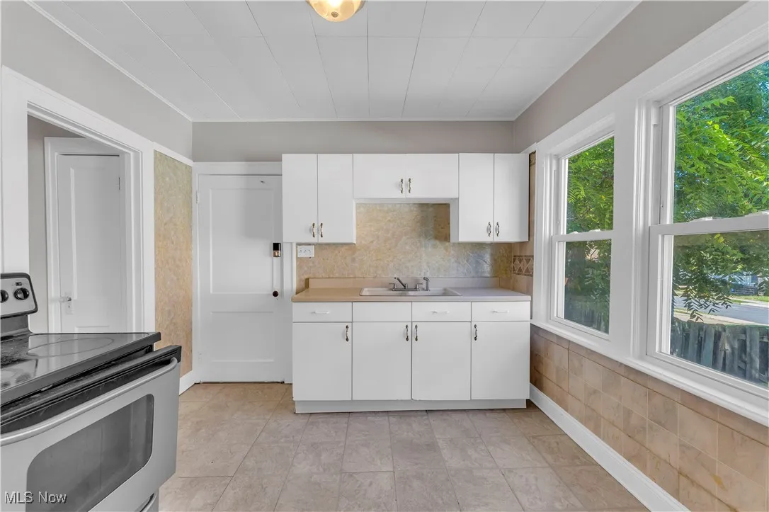 Kitchen with stainless steel electric stove, white cabinets, light countertops, and backsplash