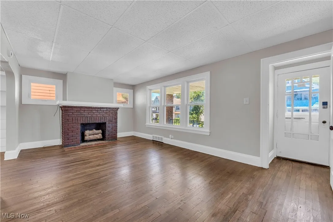 Unfurnished living room with dark wood finished floors, a fireplace, healthy amount of natural light, and a paneled ceiling